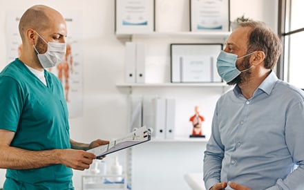 A physical therapist talking to a patient, wearing masks.