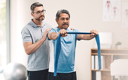 A physical therapist leads a man through strengthening exercises using an elastic band.