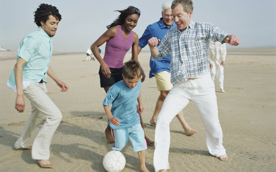 A mixed race family enjoying a game of soccer on the beach.