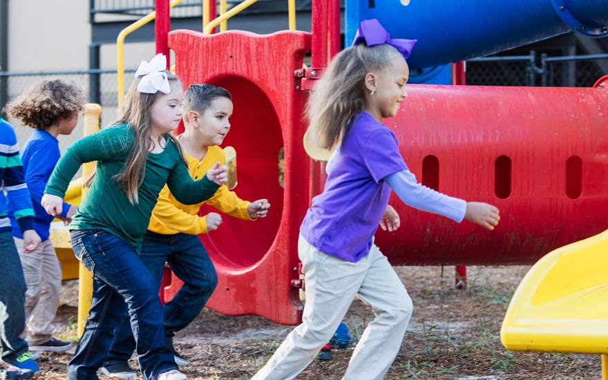 A child with down syndrome playing on the playground with friends.