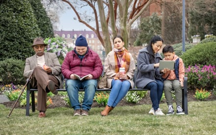 An older adult, man with down syndrome, a woman, and a mother with son sitting on a park bench.