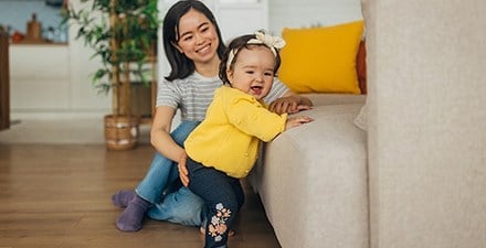 An infant cruises a couch while her mom guides her