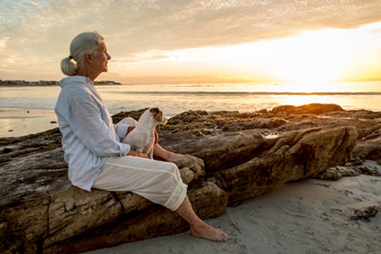Older adult woman sitting on rocks.
