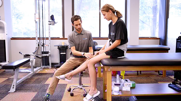 A physical therapist examines a young girl's knee.