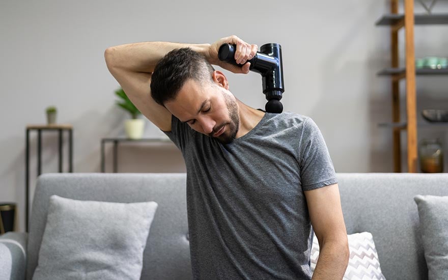 A man using a massage gun on the muscles between his neck and shoulder
