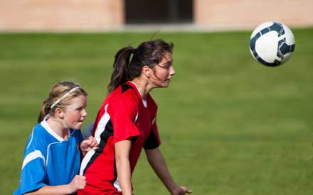 A young female athlete heads a soccer ball during a game.