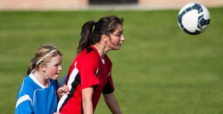 A young female athlete heads a soccer ball during a game.