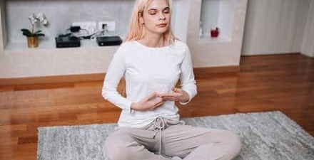 A woman does deep breathing and meditation while sitting on her bed.