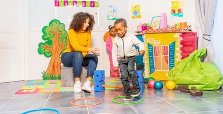 A child jumps from hoop to hoop as classmates, teacher looks on.