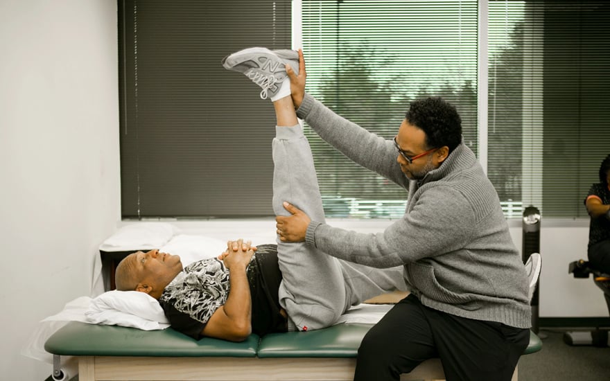 A black PT helps a black patient with flexibility exercises.