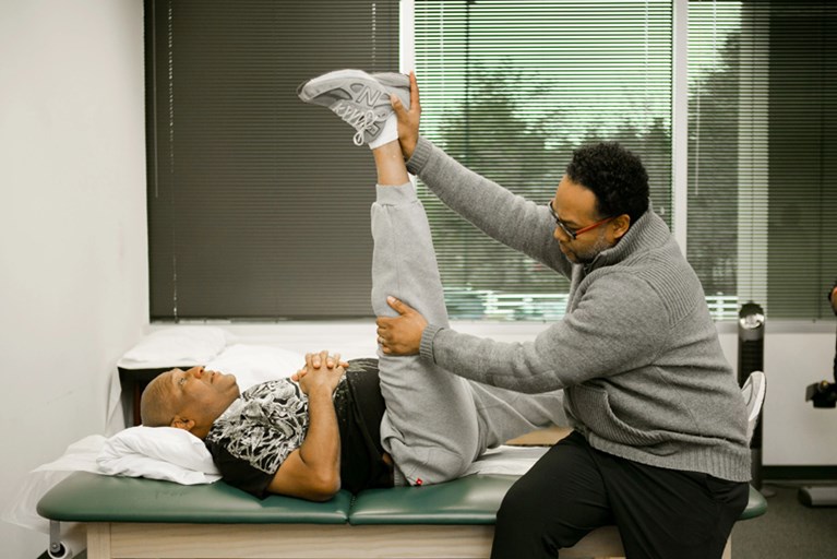 A black PT helps a black patient with flexibility exercises.