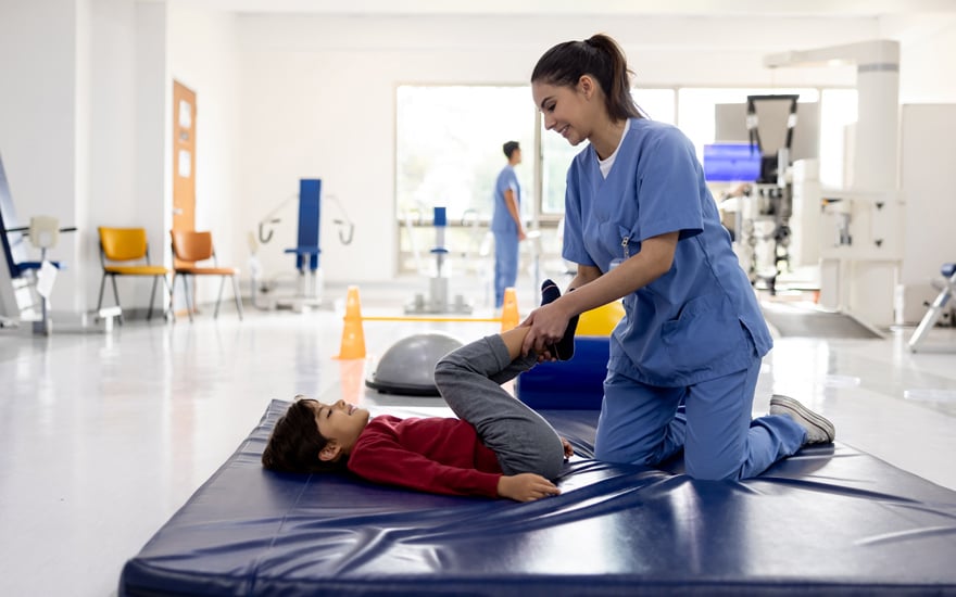 A physical therapist provides gentle stretching for a child's leg joints.