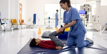 A physical therapist provides gentle stretching for a child's leg joints.