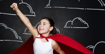 A girl in a cape with arm out and hand clenched looking like she is preparing to fly.