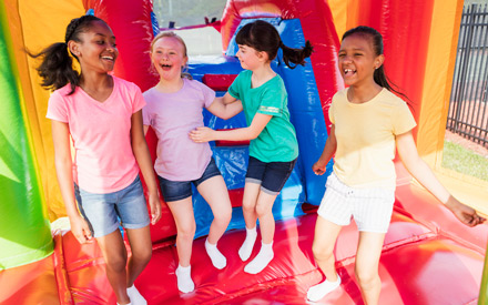 A girl with Down syndrome jumping in a bouncy house with friends.