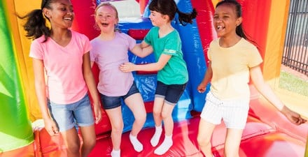 A girl with Down syndrome jumping in a bouncy house with friends.