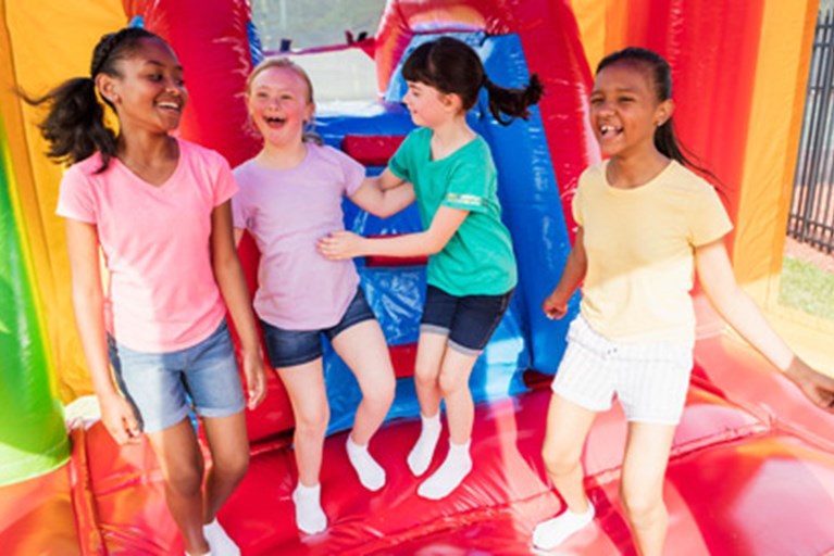 A girl with Down syndrome jumping in a bouncy house with friends.