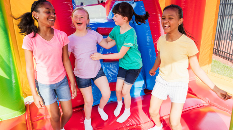 A girl with Down syndrome jumping in a bouncy house with friends.