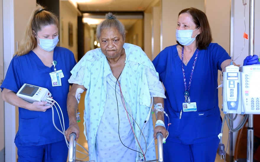 A hospital patient walks with the help of physical therapists