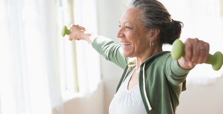 An adult female lifting light weights and smiling