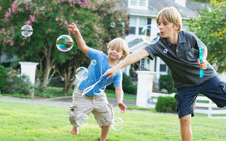 A boy with down syndrome and his brother playing outdoors with bublbles.