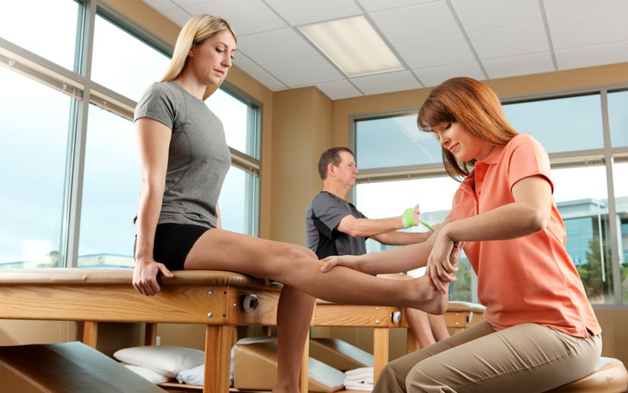 A physical therapist performs strength testing on a woman's ankle.