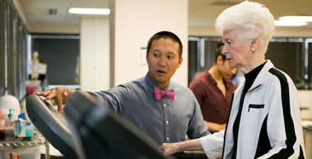 A physical therapist monitors an older adult walking on a treadmill.