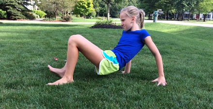 A young person doing the crab walk activity on the grass 