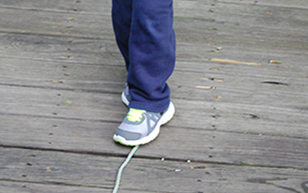 A child doing a "tight rope" walk over a string on the ground.
