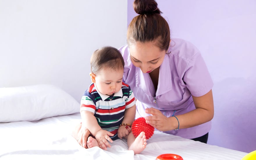 A physical therapist uses a bright ball to encourage an infant to move.