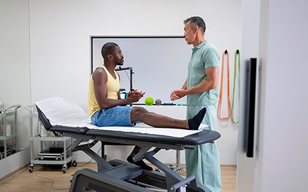 A PT educates a patient who is sitting on a treatment table about his leg.