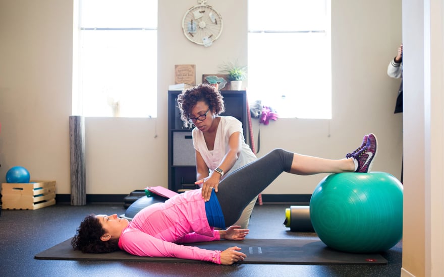 A physical therapist helping a patient do a bridge exercise on a therapy ball.