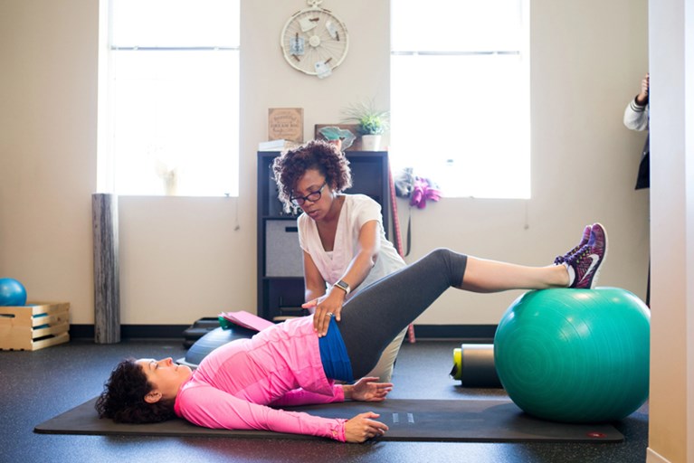 A physical therapist helping a patient do a bridge exercise on a therapy ball.