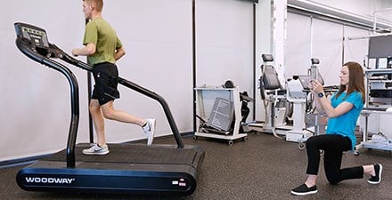 A physical therapist assesses foot stability while a patient runs on a treadmill