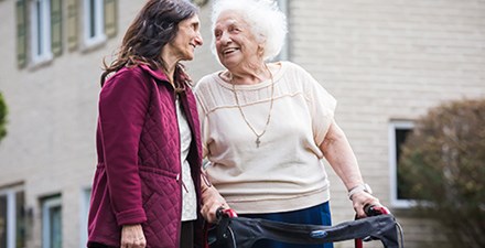 Virginia, using a walker outdoors, smiling toward another woman.