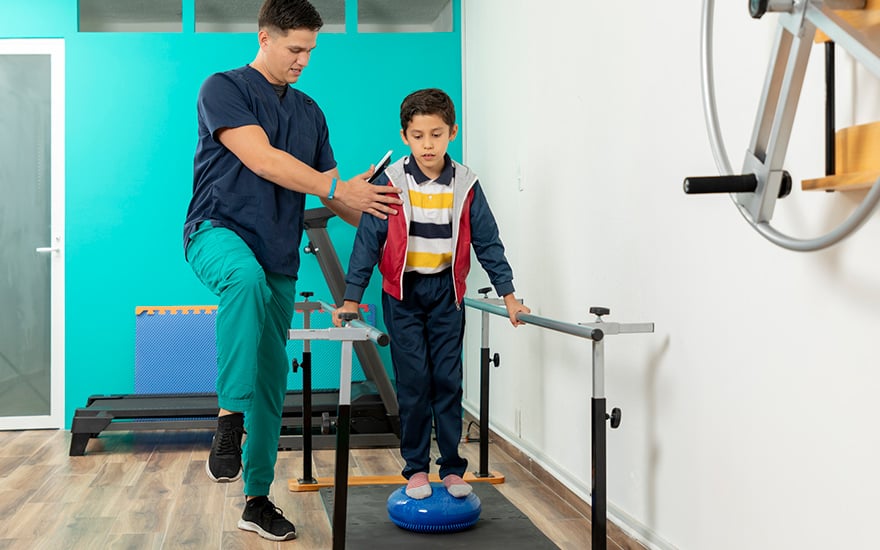 A physical therapist works with a young boy on balance and leg strengthening