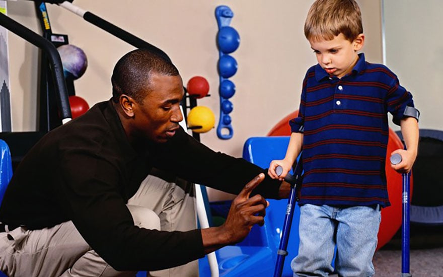 A physical therapist instructs a young boy on the use of a Lofstrand crutches