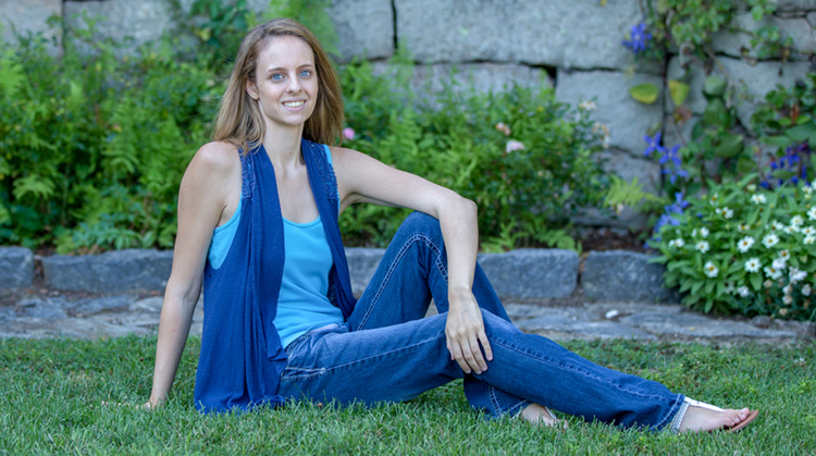 Margaret, a young woman, sitting on the grass smiling at the camera.