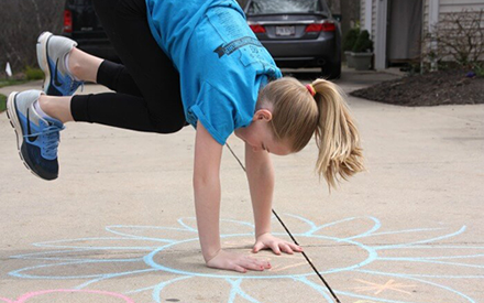 A child with her hands on the ground and feet in the air on a chalk drawing of a posie.