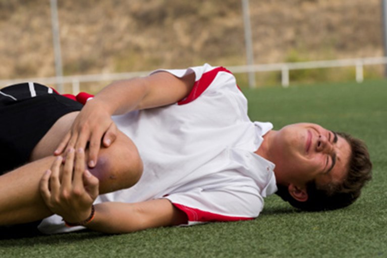 Youth athlete with a knee injury holds his knee on the soccer field.