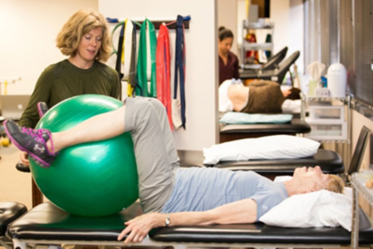 A physical therapist works with a patient using an exercise ball to strengthen their core.