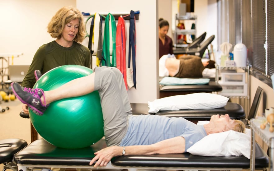 A physical therapist works with a patient using an exercise ball to strengthen their core.