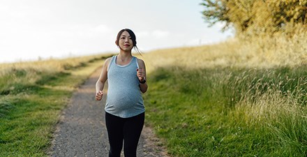 A pregnany woman walking briskly on an outdoor trail.