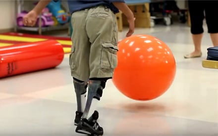 A boy with muscular dystrophy chasing a ball in a physical therapy clinic.