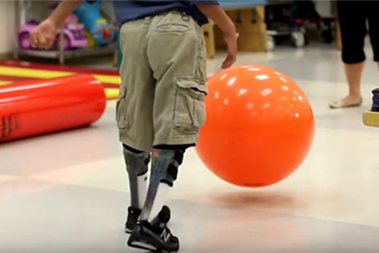 A boy with muscular dystrophy chasing a ball in a physical therapy clinic.