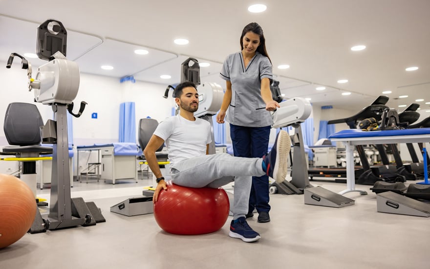 A physical therapist guides a man through leg strengthening exercises.