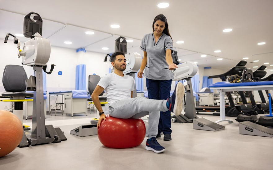 A physical therapist guides a man through leg strengthening exercises.