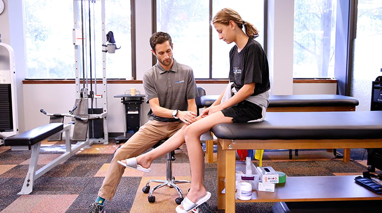 A physical therapist working with a young teen on her knee