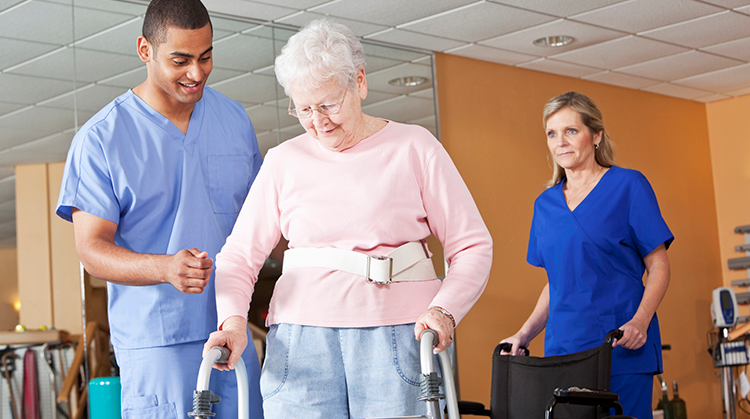 A physical therapist helping a women learn to walk usins a walker