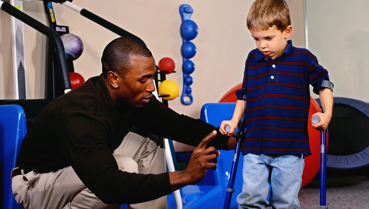 A physical therapist teaches a young child to use arm crutches